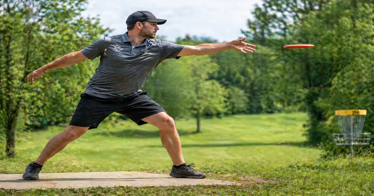A disc golfer mid-backhand throw with arm extended at release point